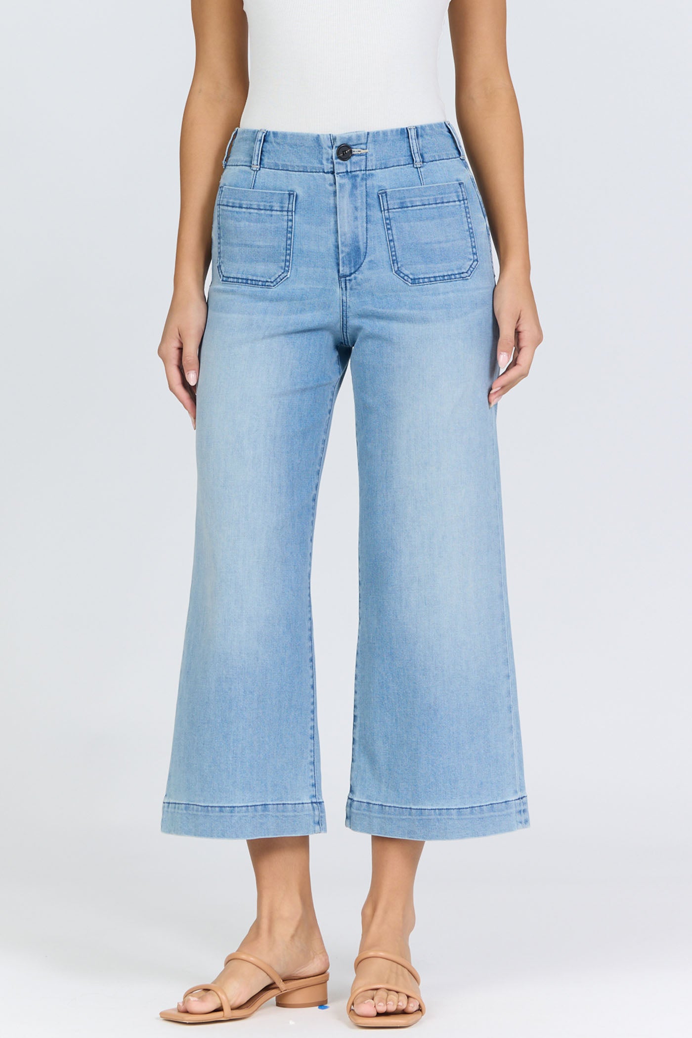 Front view of a woman wearing light-wash high-rise wide-leg cropped jeans with front patch pockets and tan slide sandals.