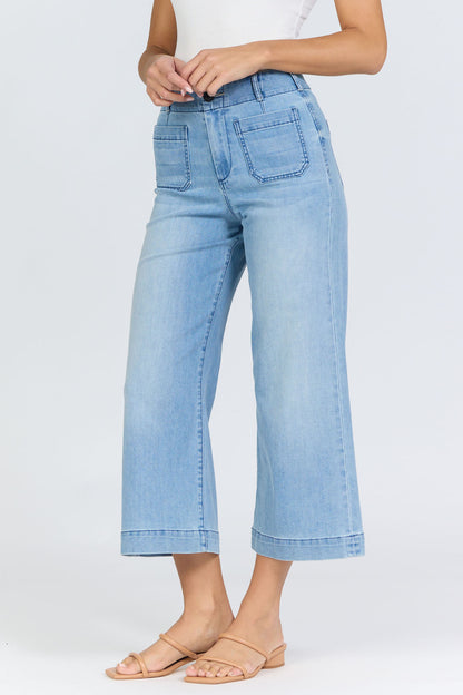 Side view of a woman wearing light-wash high-rise wide-leg cropped jeans with front patch pockets and tan slide sandals.