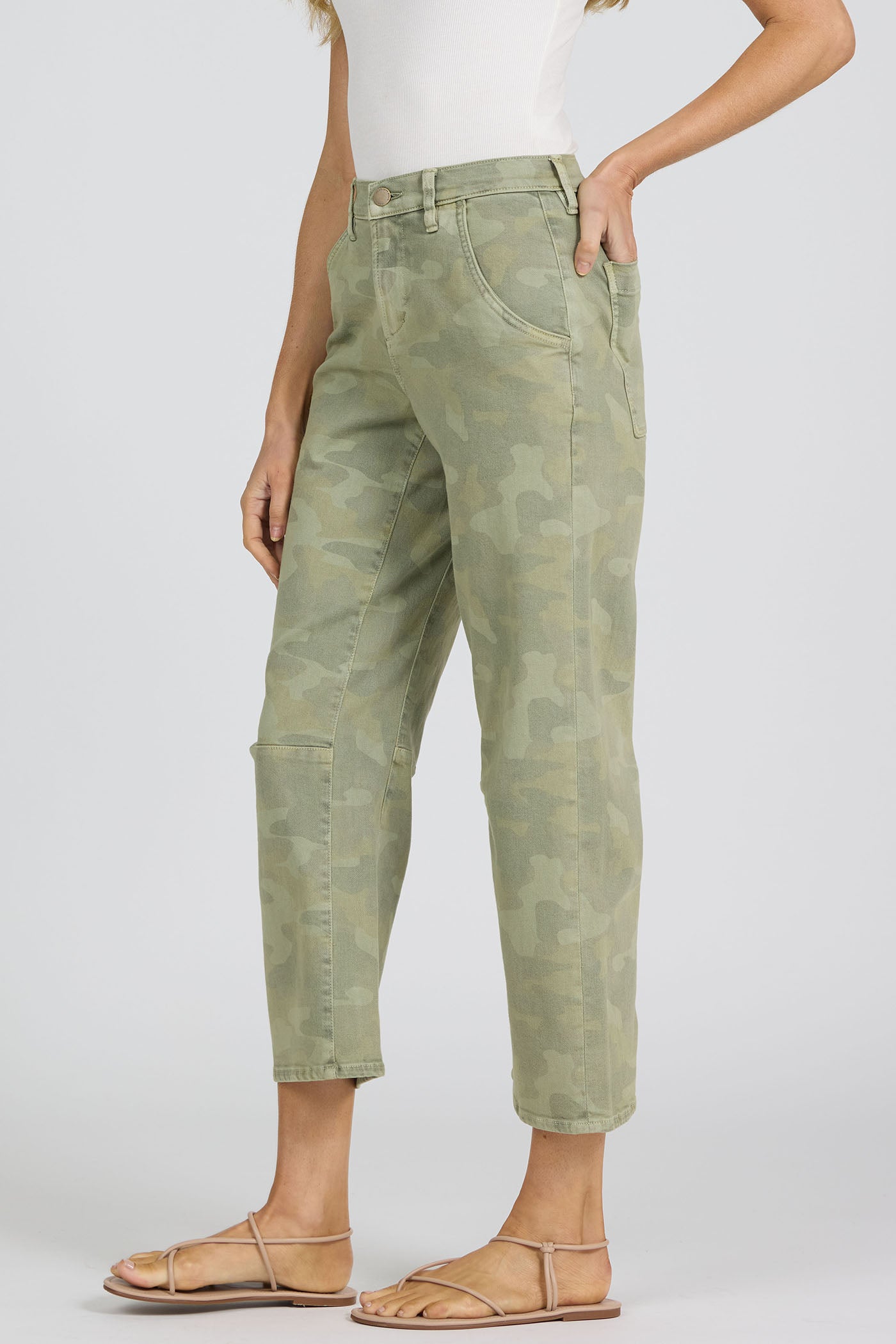 Side view of a woman wearing green camouflage pants on a white background.
