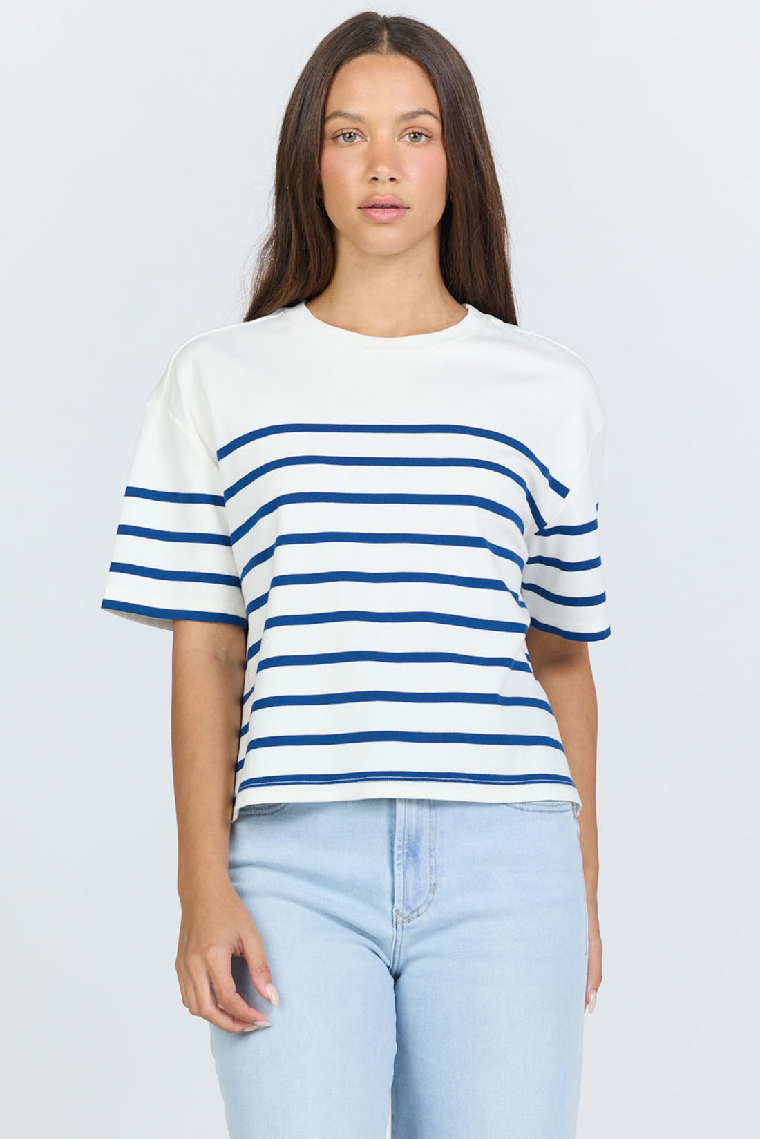 Front view of a woman wearing a white and blue horizontal striped crew neck cotton t-shirt with light-wash jeans.