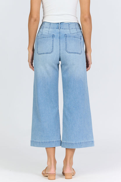 Rear view of a woman wearing light-wash high-rise wide-leg cropped jeans with front patch pockets and tan slide sandals.