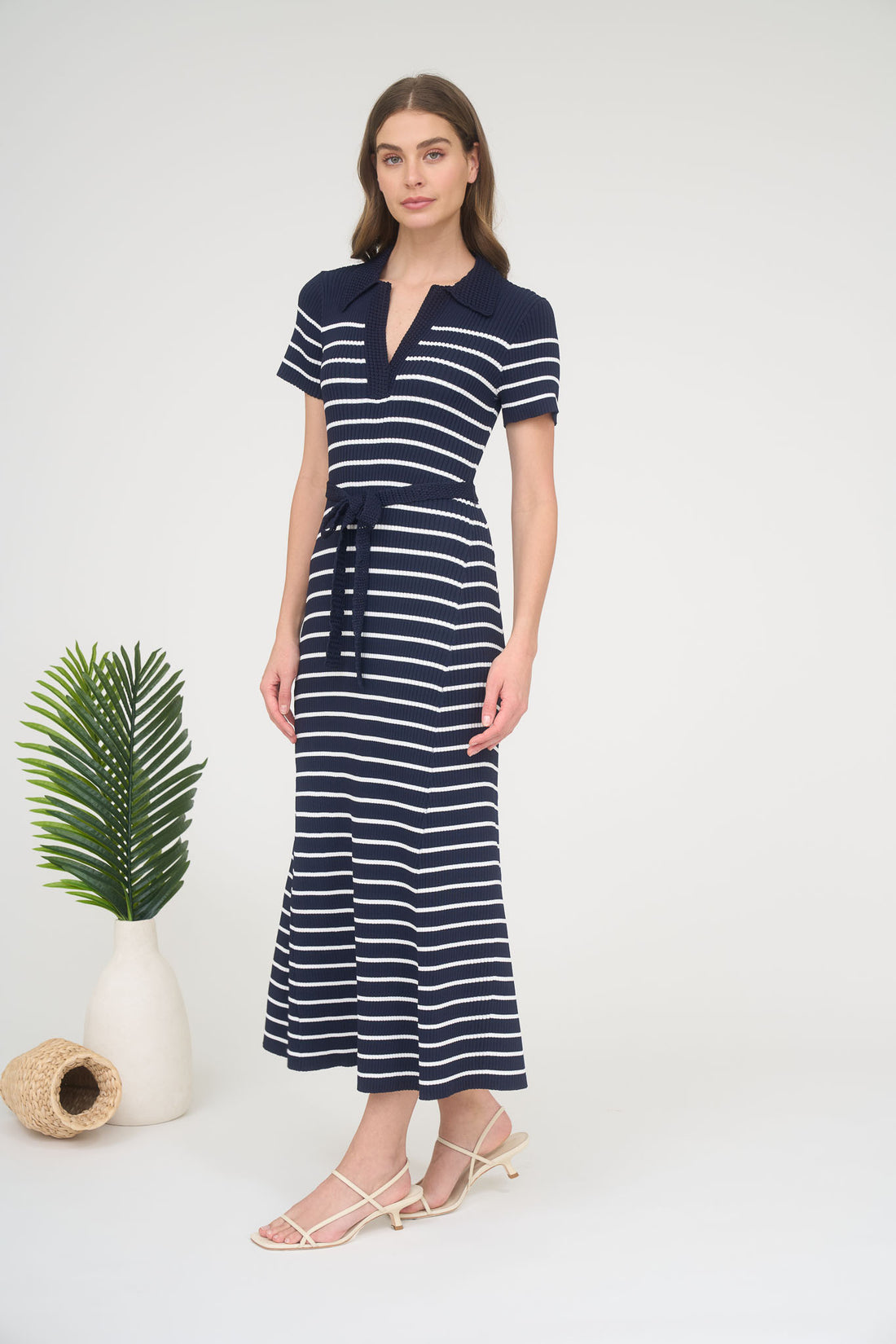 A woman wearing a short-sleeve navy and white horizontally striped ribbed knit maxi dress with a spread collar, split neck, and matching tie belt.