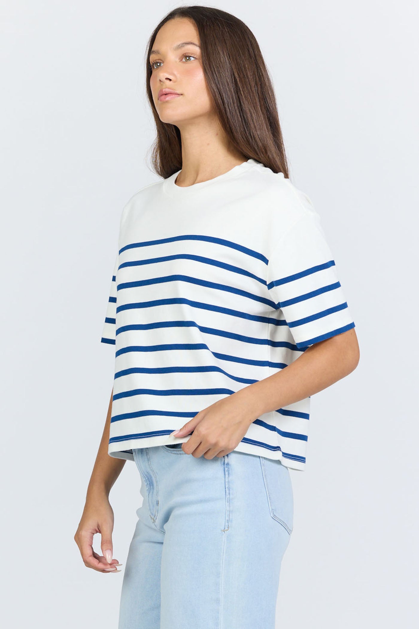 Side view of a woman wearing a white and blue horizontal striped crew neck cotton t-shirt with light-wash jeans.