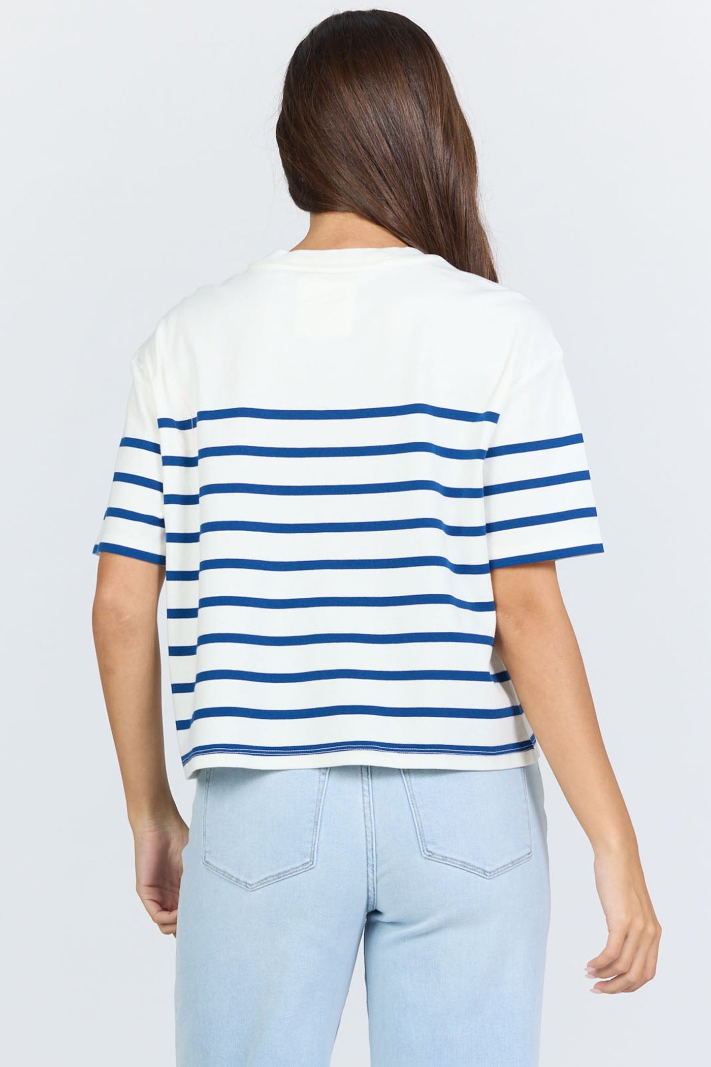 Rear view of a woman wearing a white and blue horizontal striped crew neck cotton t-shirt with light-wash jeans.