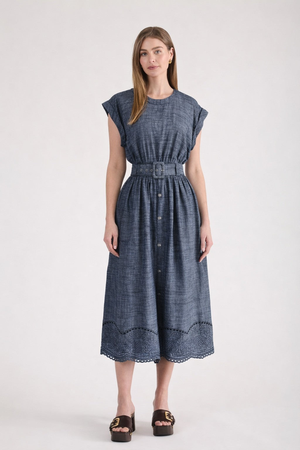 A woman wearing a short-sleeve chambray midi dress with a wide grommet belt, a gathered waist, and an intricate floral eyelet scalloped hem.