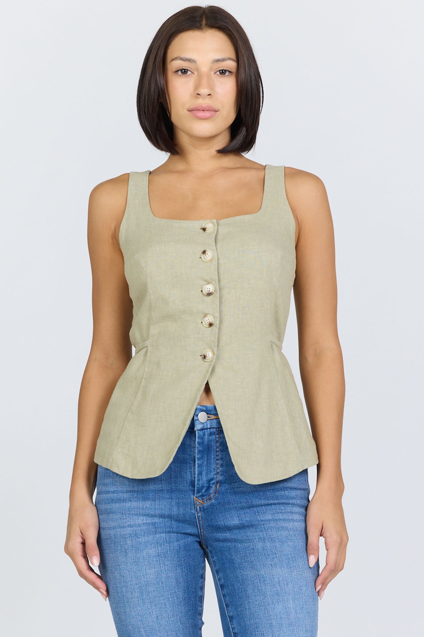 Front view of a woman wearing a sage green linen-blend sleeveless vest with a button front and blue jeans.