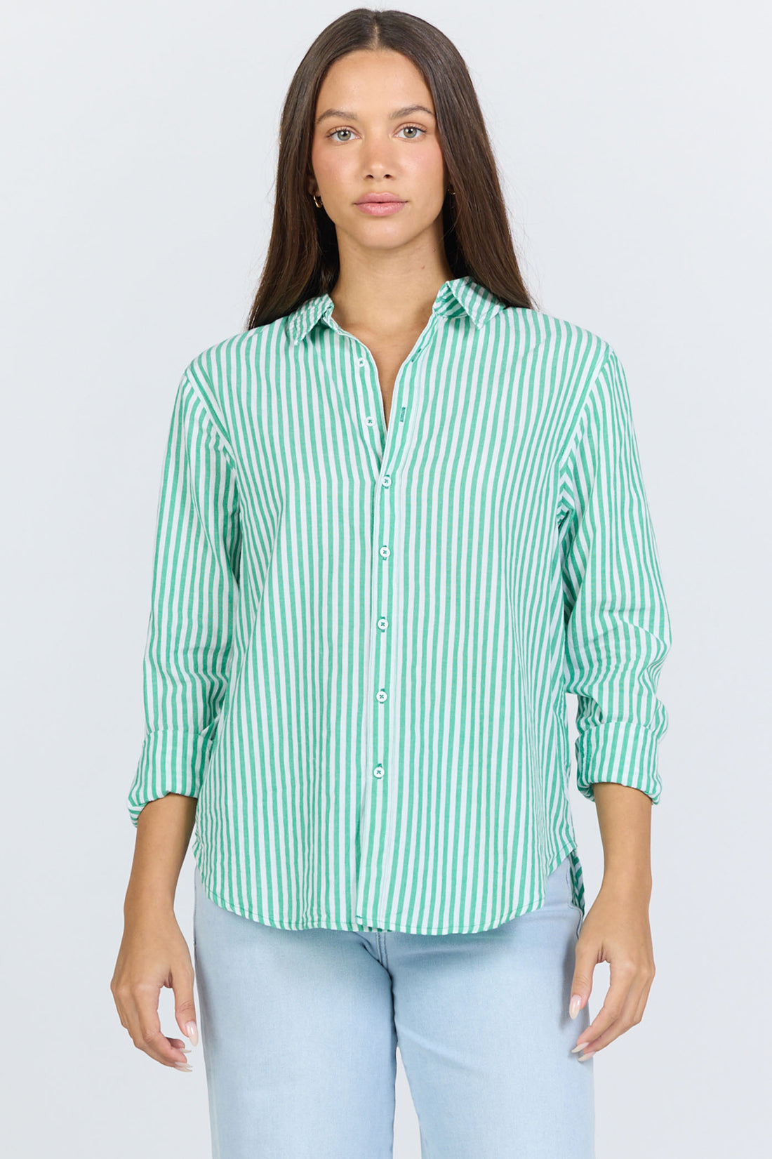 Front view of a woman wearing a green and white vertical striped long-sleeve cotton button-up shirt with light blue jeans.