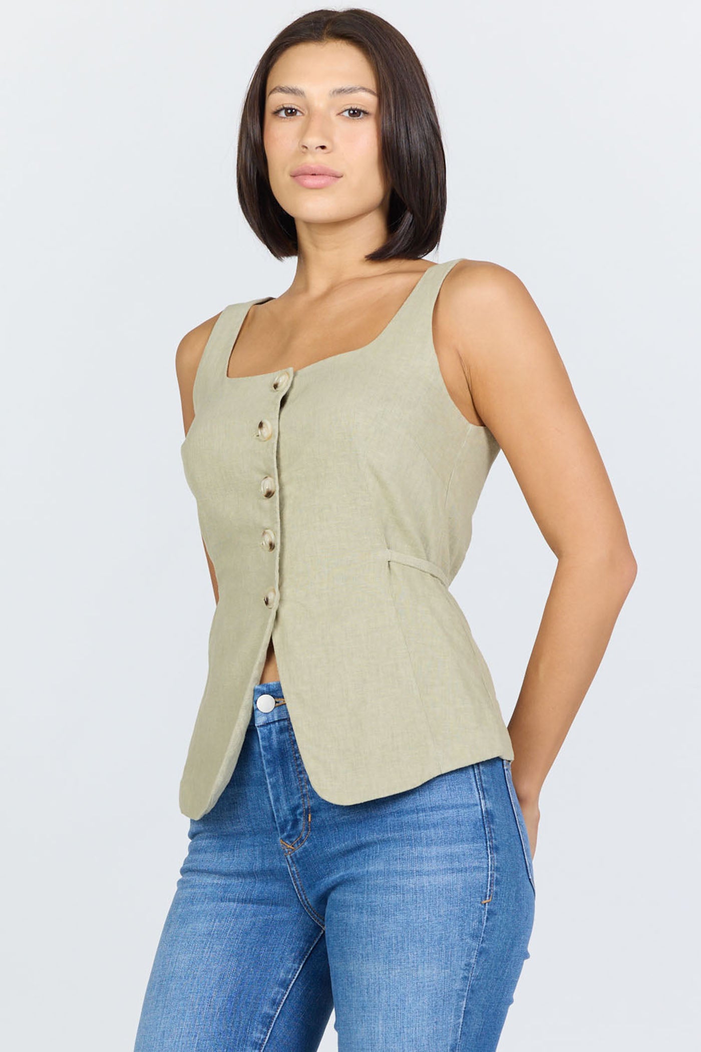 Side view of a woman wearing a sage green linen-blend sleeveless vest with a button front and blue jeans.