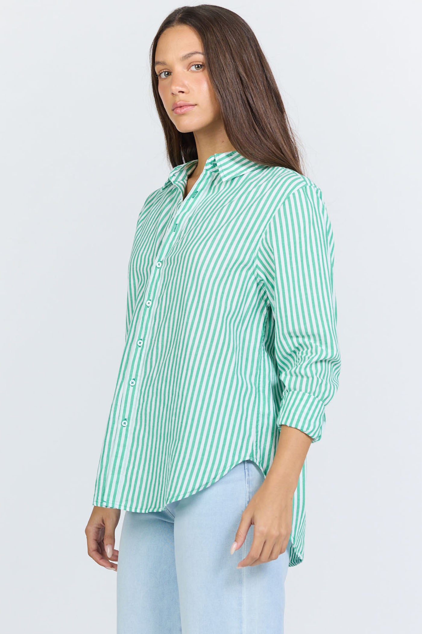 Side view of a woman wearing a green and white vertical striped long-sleeve cotton button-up shirt with light blue jeans.