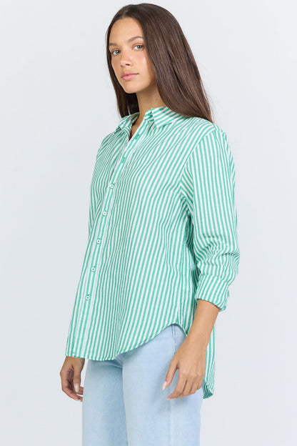 Side view of a woman wearing a green and white vertical striped long-sleeve cotton button-up shirt with light blue jeans.
