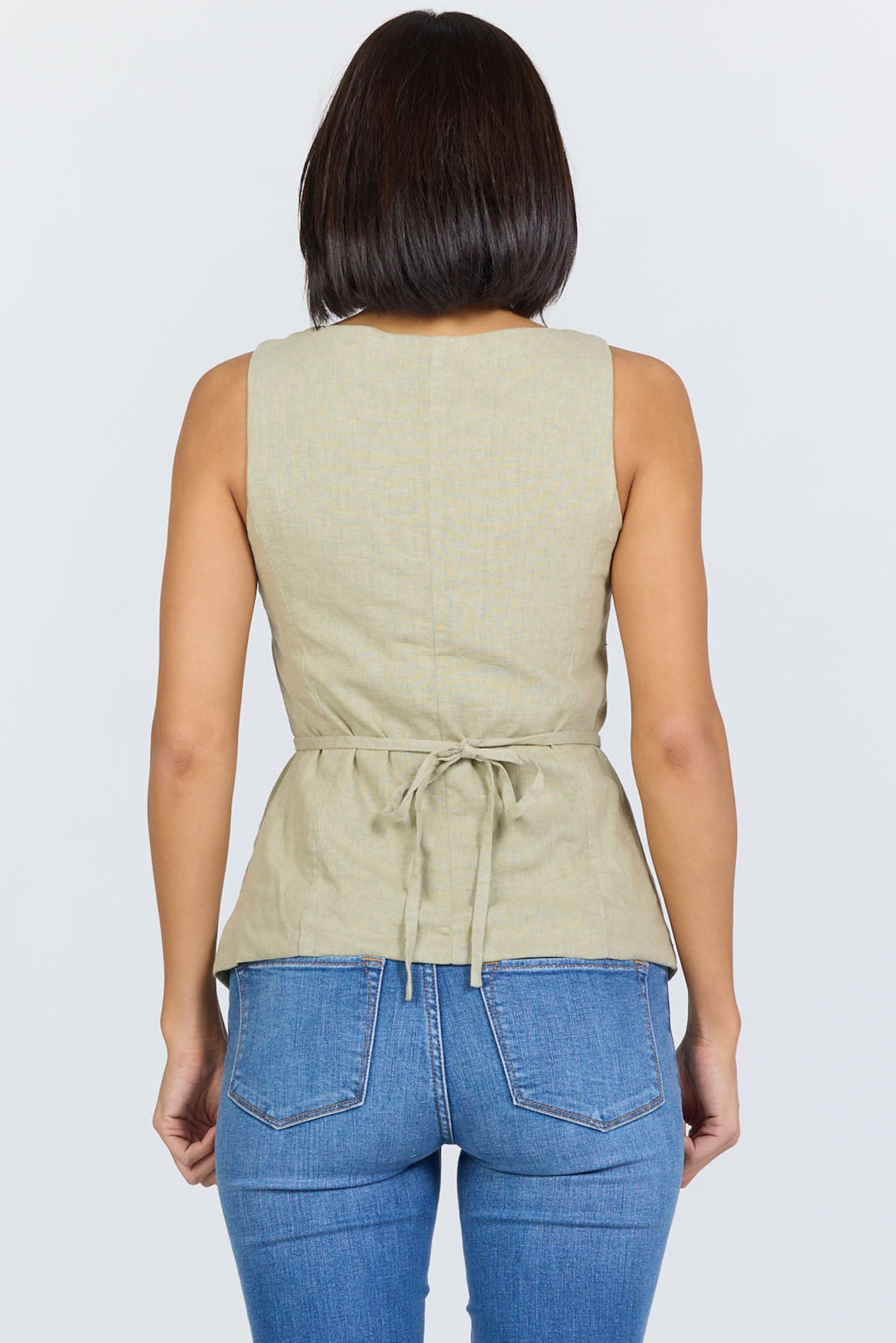 Rear view of a woman wearing a sage green linen-blend sleeveless vest with a tie back and blue jeans