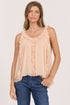 Front view of a woman wearing a flowy peach sleeveless scoop-neck top with vertical ruffles and dark blue jeans.