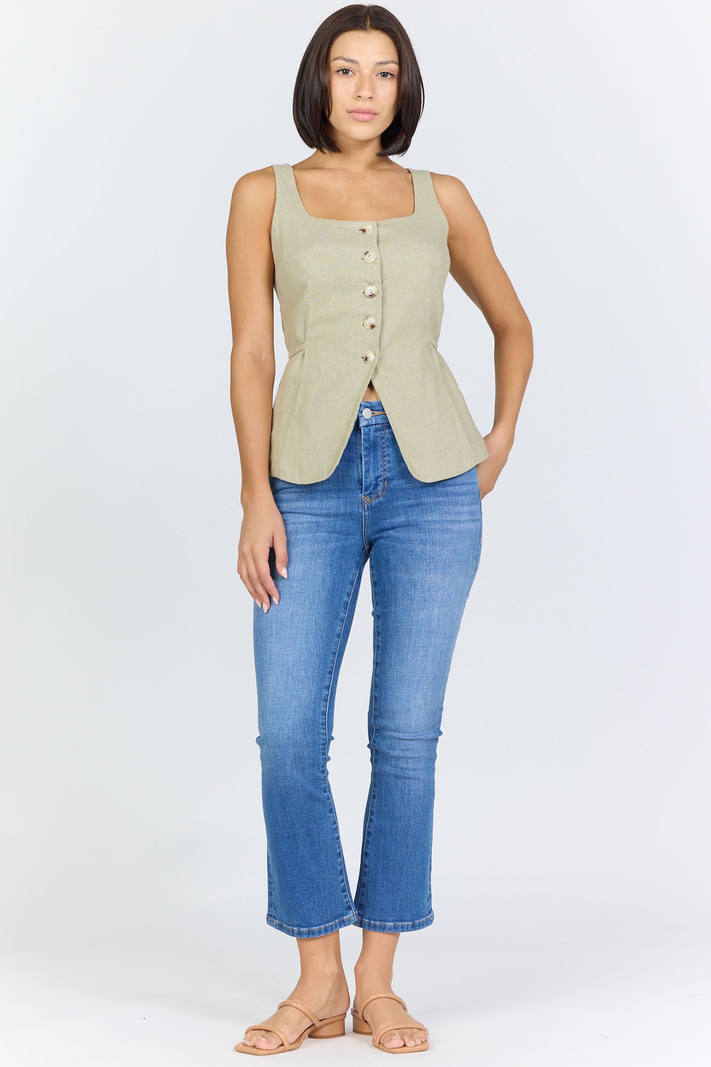 Full body view of a woman wearing a sage green linen-blend sleeveless vest with a button front and blue jeans