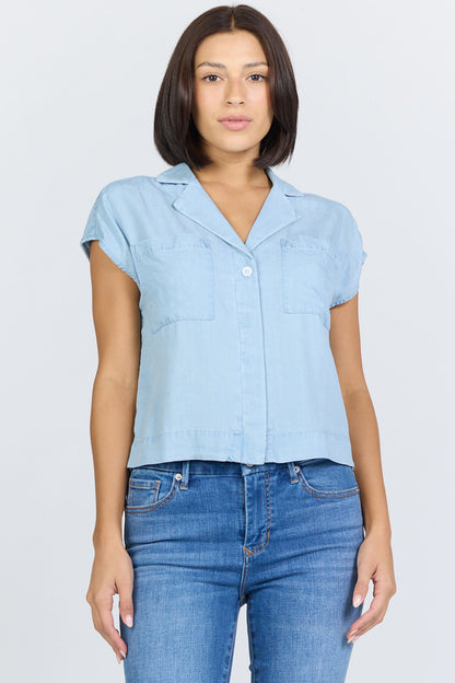 Front view of a woman wearing a light blue 100% Tencel boxy camp collar shirt with blue jeans.