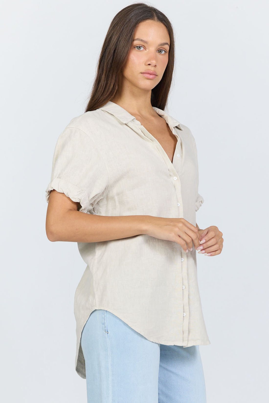 Side view of a model wearing a neutral cream linen-blend short sleeve button-down shirt with light blue jeans.