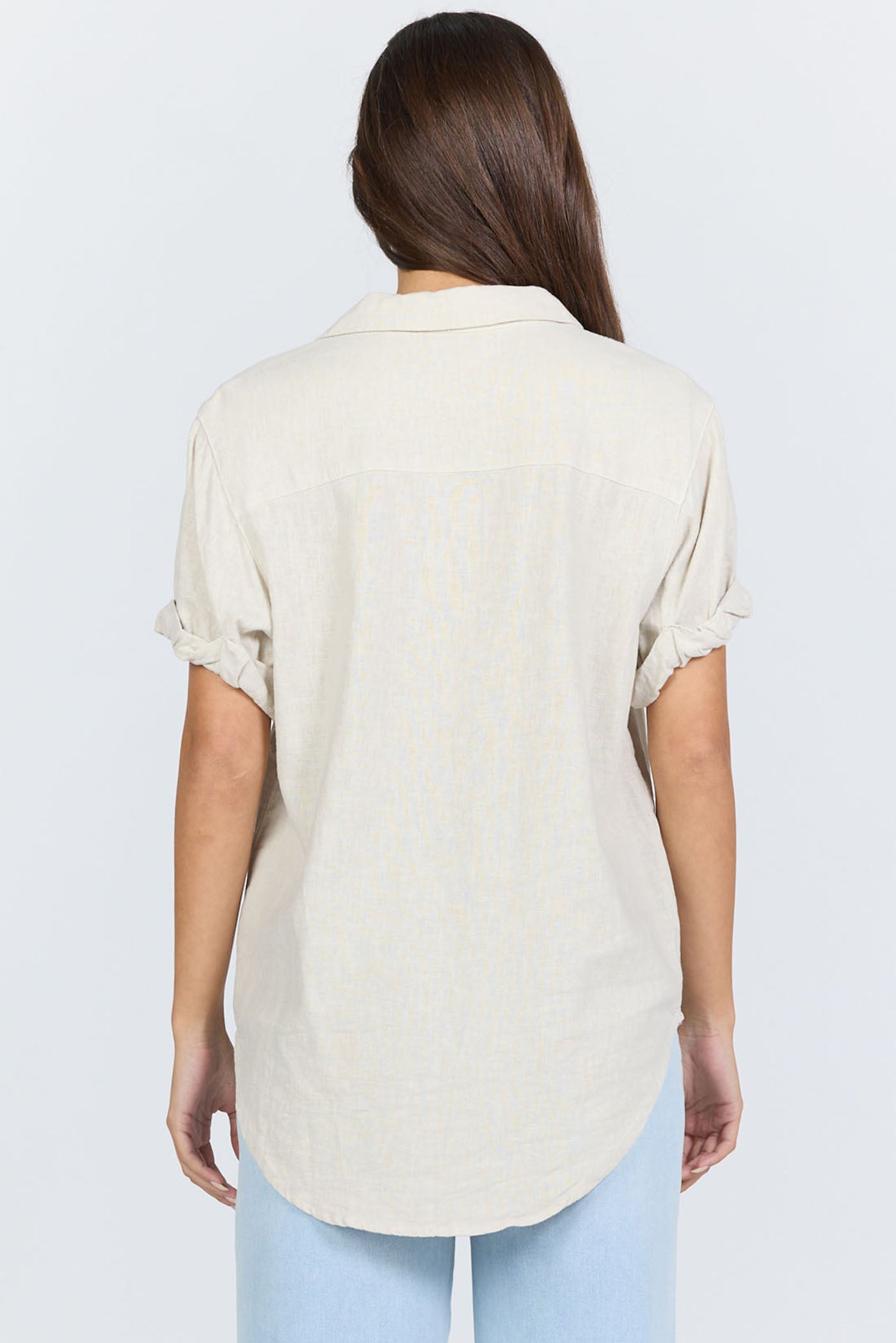 Rear view of a model wearing a neutral cream linen-blend short sleeve button-down shirt with light blue jeans.