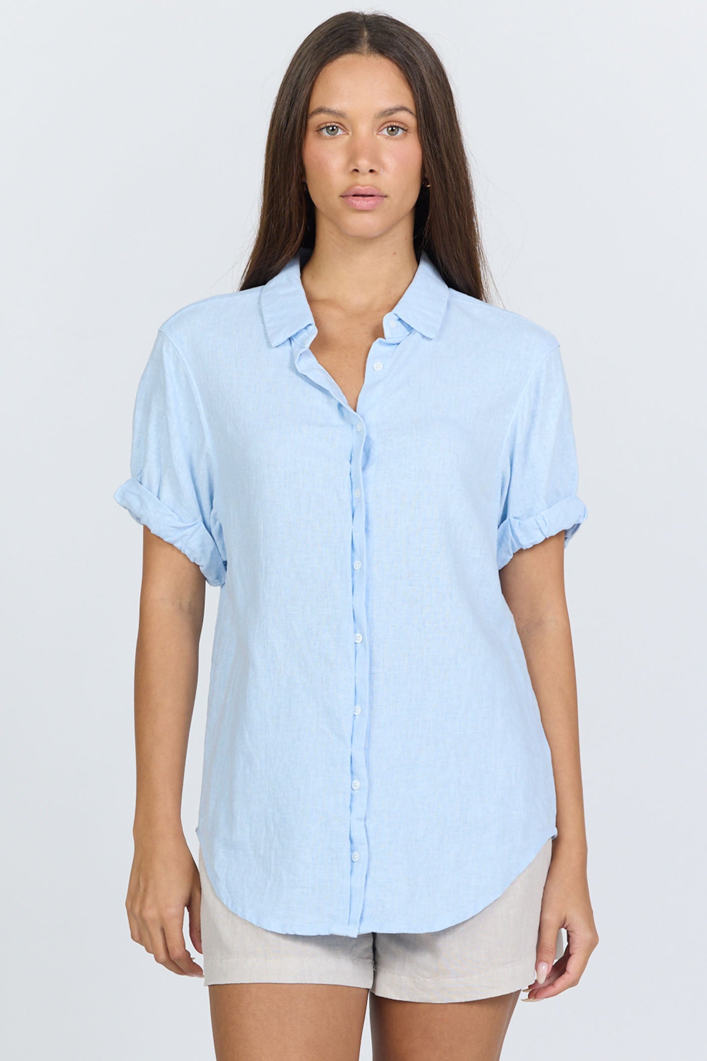 Front view of a model wearing a light blue linen-blend short sleeve button-down shirt with white trousers.