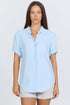 Front view of a model wearing a light blue linen-blend short sleeve button-down shirt with white trousers.