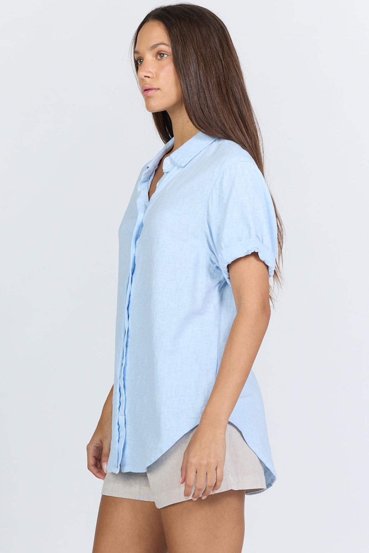 Side view of a model wearing a light blue linen-blend short sleeve button-down shirt with white trousers.