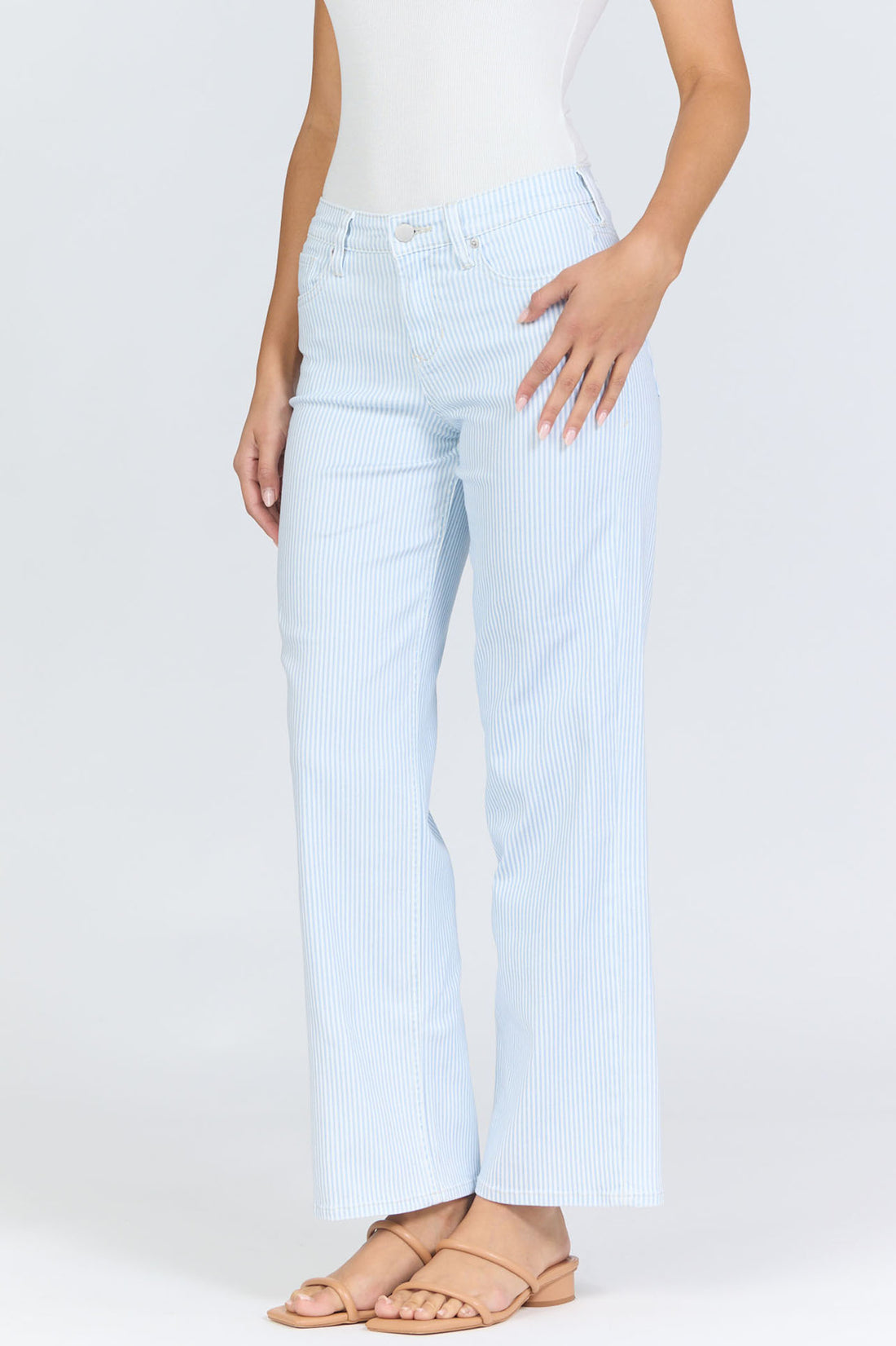 Side view of a woman wearing light blue pinstripe straight-leg jeans with a mid-high rise waistband and a white tank top.