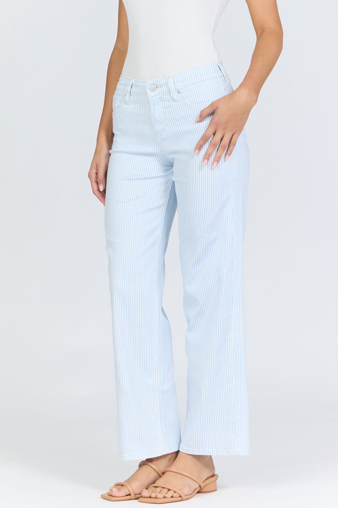 Side view of a woman wearing light blue pinstripe straight-leg jeans with a mid-high rise waistband and a white tank top.