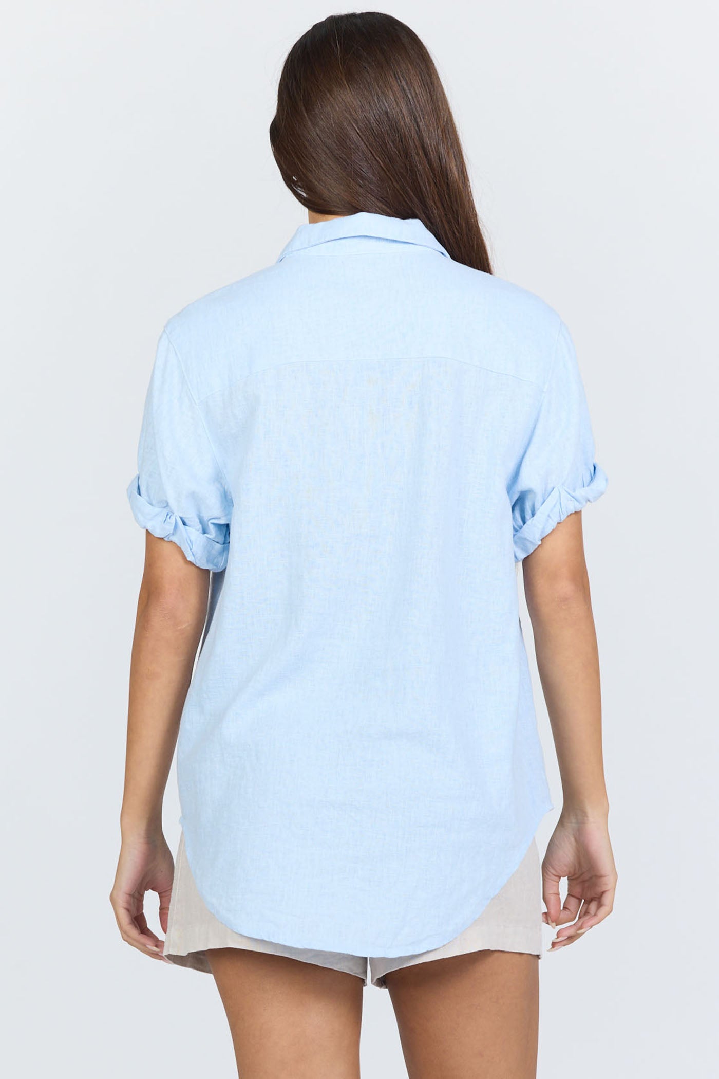 Rear view of a model wearing a light blue linen-blend short sleeve button-down shirt with white trousers.