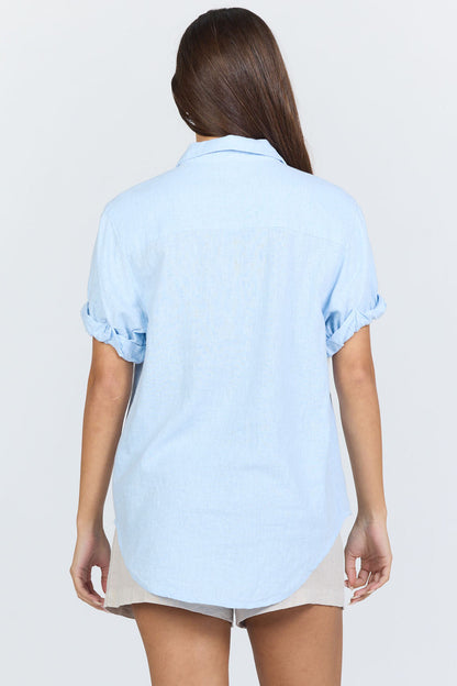 Rear view of a model wearing a light blue linen-blend short sleeve button-down shirt with white trousers.