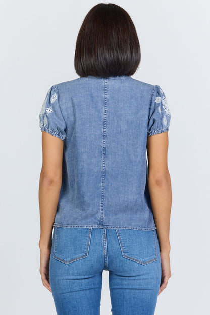 Rear view of a woman wearing a light blue 100% Tencel V-neck blouse with embroidered short puff sleeves, paired with denim jeans.