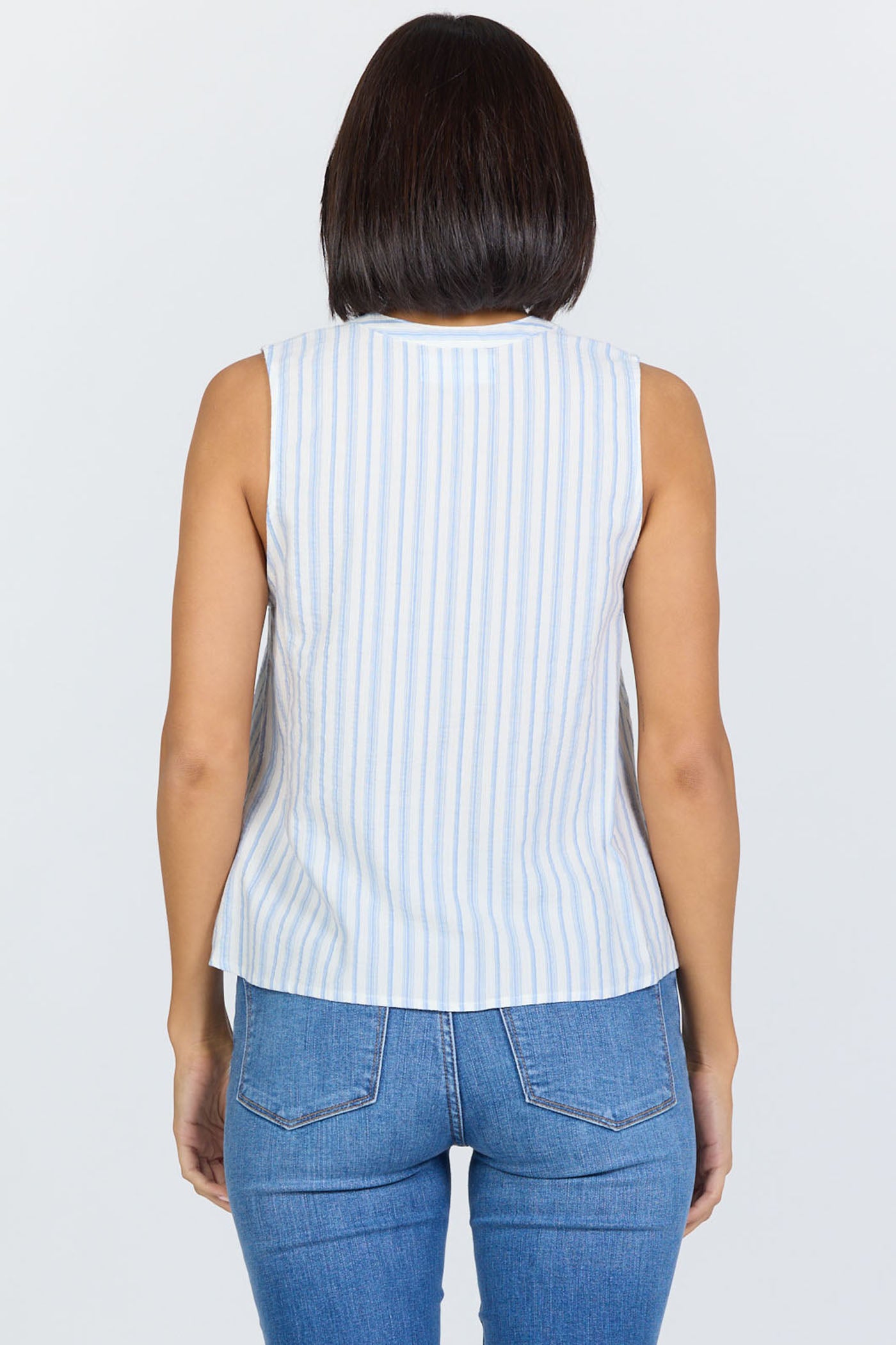 Rear view of a woman with a dark bob haircut wearing a sleeveless blue and white striped cotton-blend top with a button-up Henley neck and blue jeans.