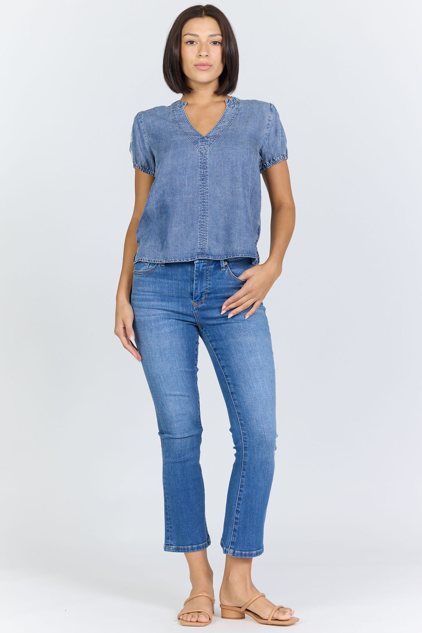 Full body view of a woman wearing a light blue 100% Tencel V-neck blouse with embroidered short puff sleeves, paired with denim jeans.