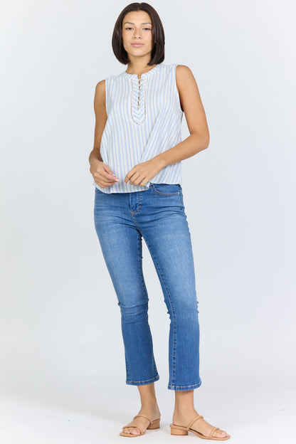 Full body view of a woman with a dark bob haircut wearing a sleeveless blue and white striped cotton-blend top with a button-up Henley neck and blue jeans.