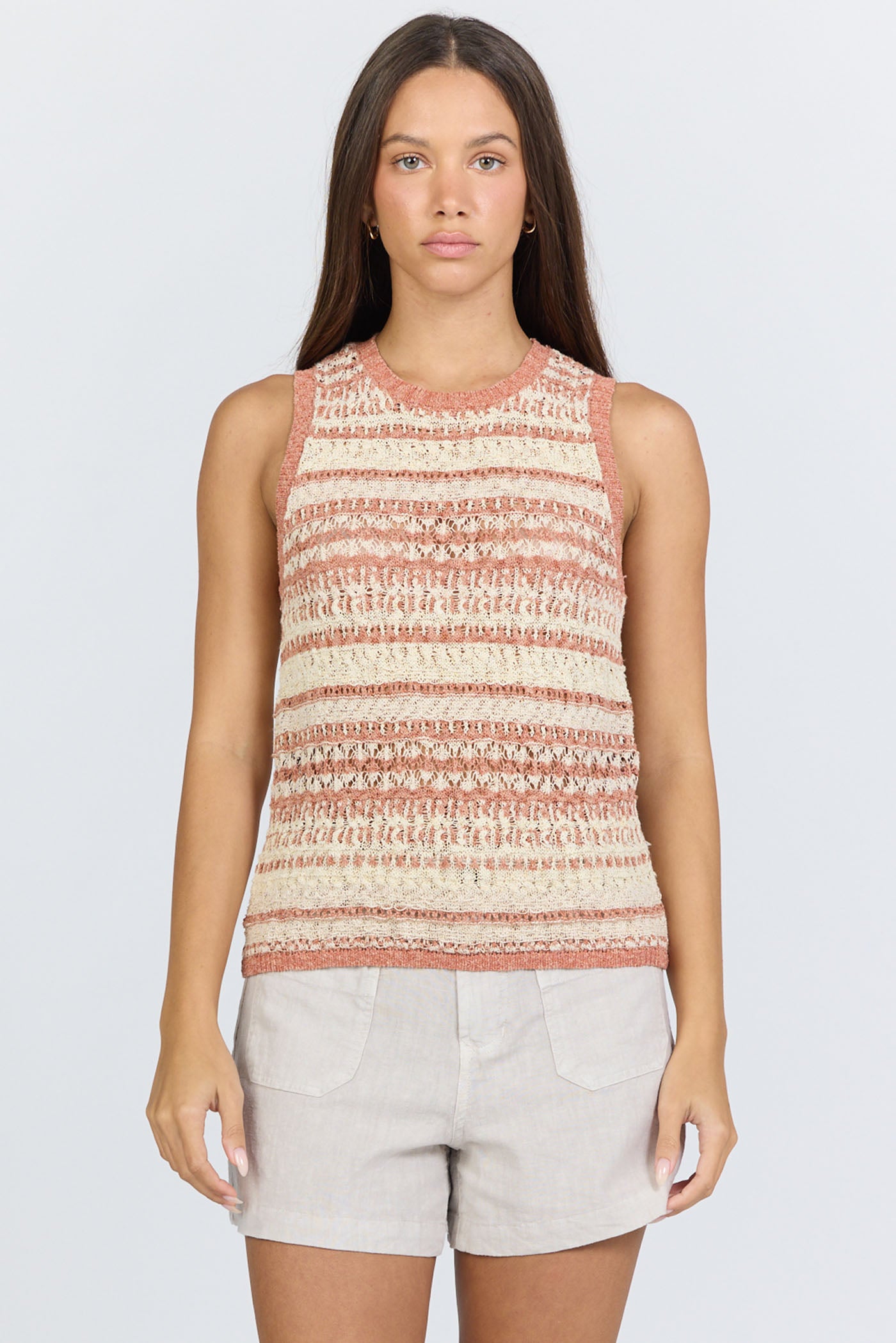 Front view of a woman wearing a sleeveless crew-neck sweater tank with terra-cotta and ivory horizontal stripes, paired with light linen shorts.