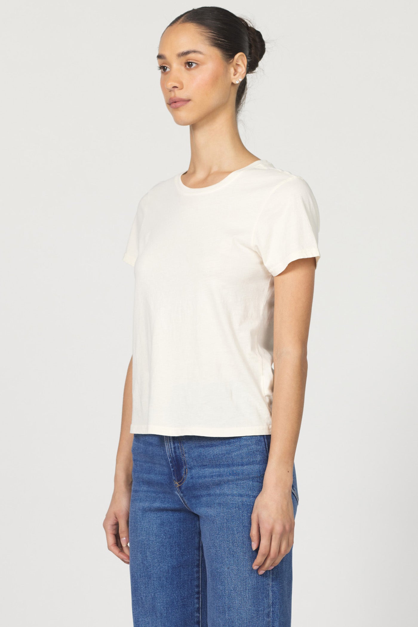 Side view of a woman wearing a white classic short-sleeve crew neck cotton jersey t-shirt paired with denim