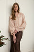 A woman wearing a romantic, flowy blush pink long-sleeve blouse featuring intricate tiered pleats on the sleeves and a gold-buttoned neckline.