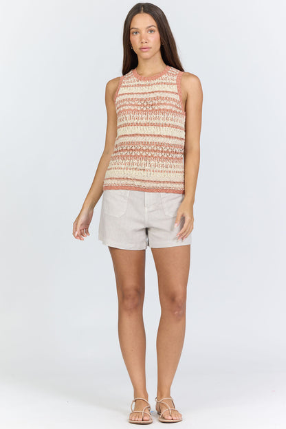 Full body view of a woman wearing a sleeveless crew-neck sweater tank with terra-cotta and ivory horizontal stripes, paired with light linen shorts.