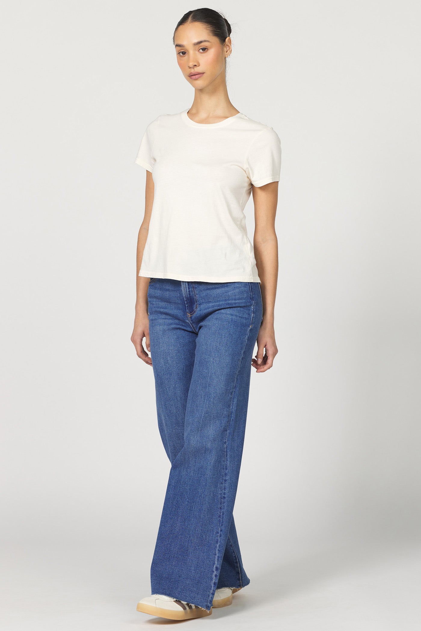 Full body view of a woman wearing a white classic short-sleeve crew neck cotton jersey t-shirt paired with denim
