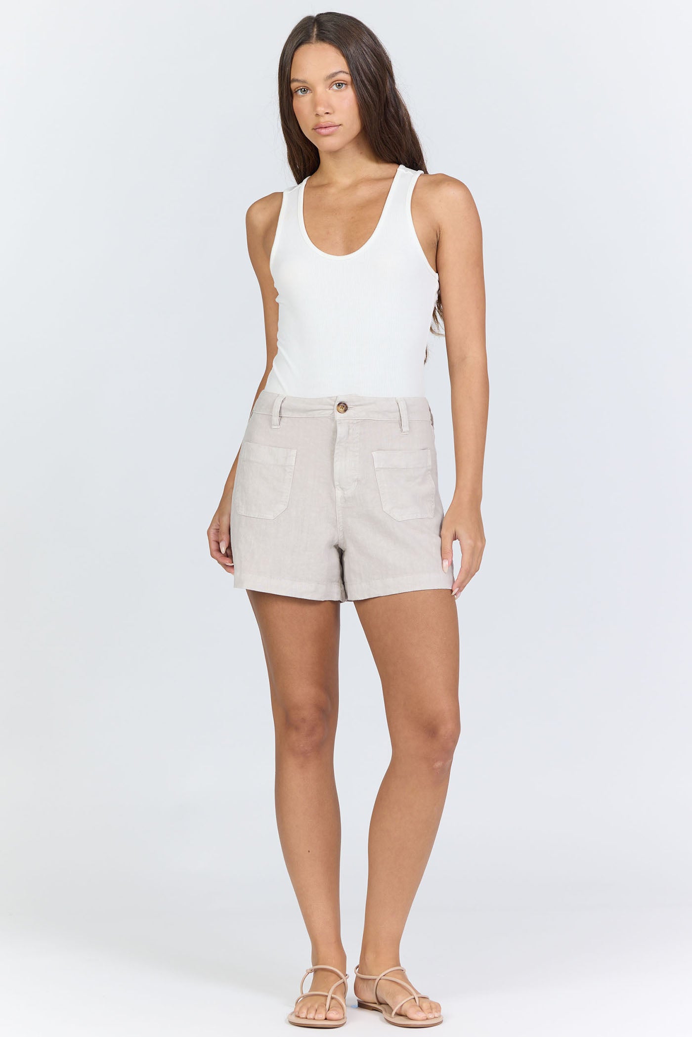 Full body view of a woman wearing oatmeal-colored high-rise linen-blend shorts with patch pockets and matching tan strappy sandals.