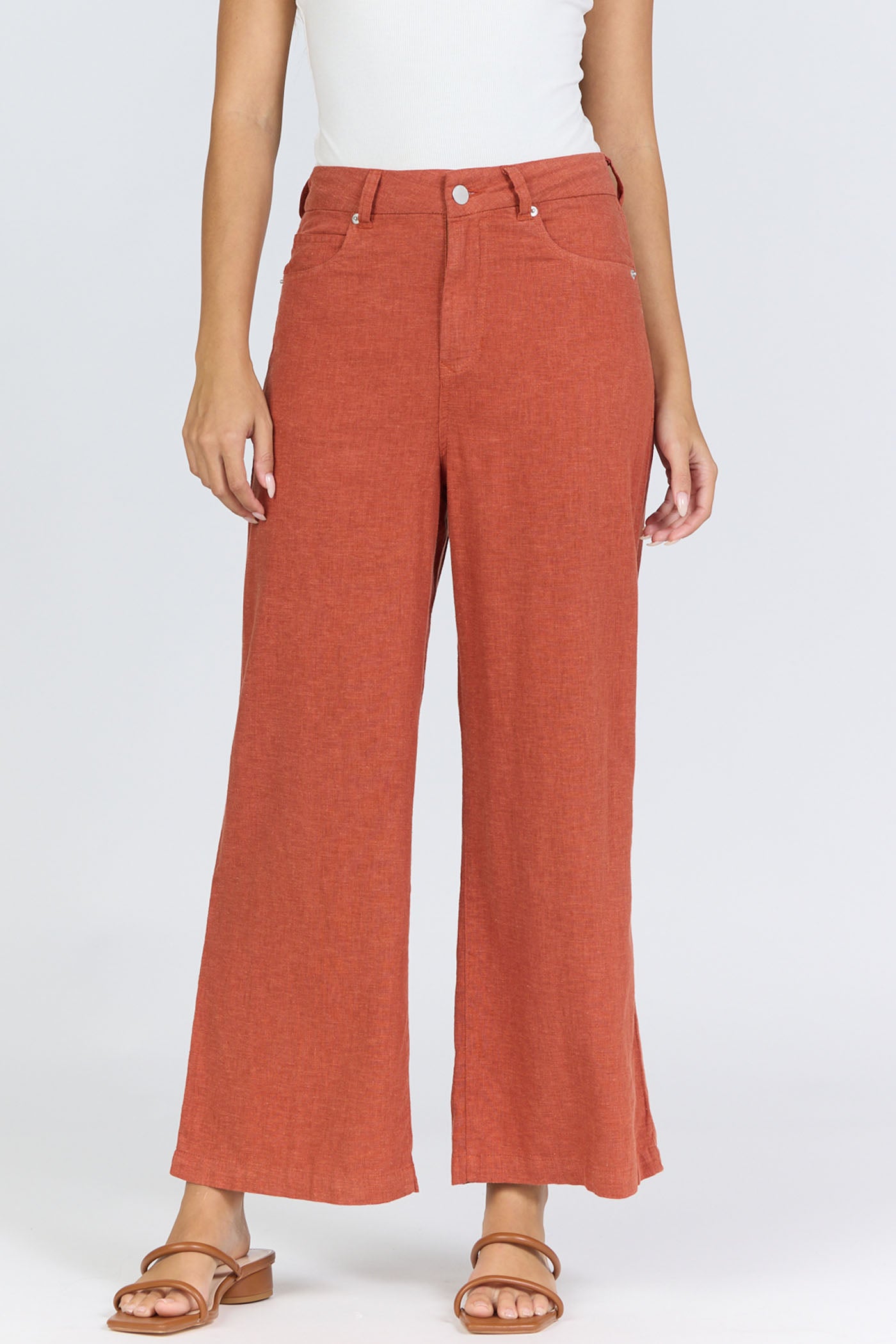 Front view of a woman wearing terracotta-colored high-rise wide-leg linen-blend pants with tan slide sandals.