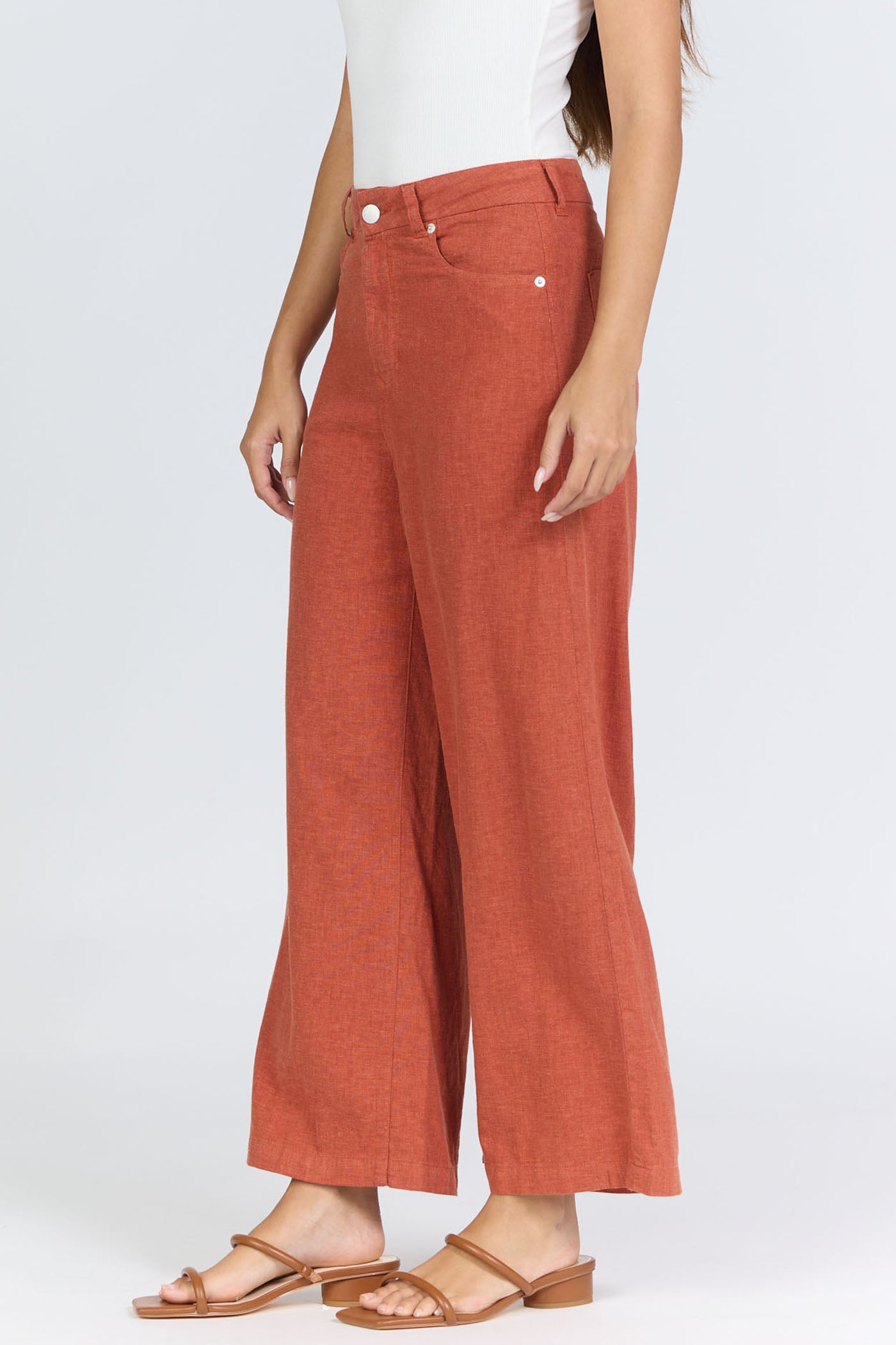 Side view of a woman wearing terracotta-colored high-rise wide-leg linen-blend pants with tan slide sandals.