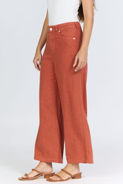 Side view of a woman wearing terracotta-colored high-rise wide-leg linen-blend pants with tan slide sandals.