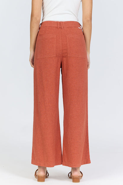 Rear view of a woman wearing terracotta-colored high-rise wide-leg linen-blend pants with tan slide sandals.