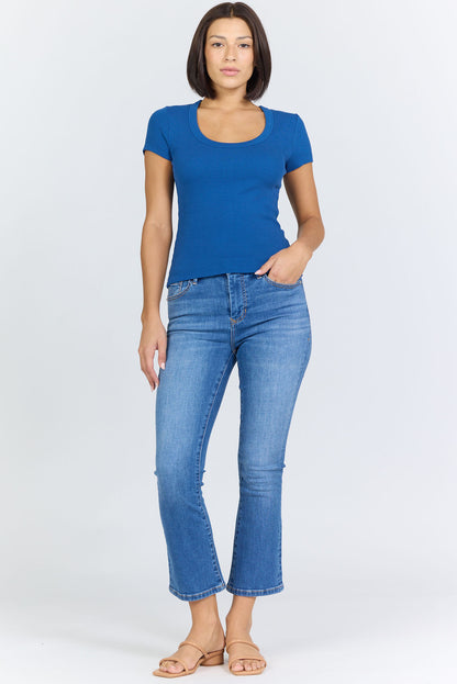 Full height view of a woman wearing a fitted blue scoop-neck short-sleeve t-shirt tucked into blue jeans.