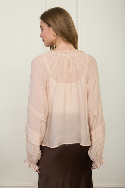 Rear view of a woman wearing a romantic, flowy blush pink long-sleeve blouse featuring intricate tiered pleats on the sleeves.