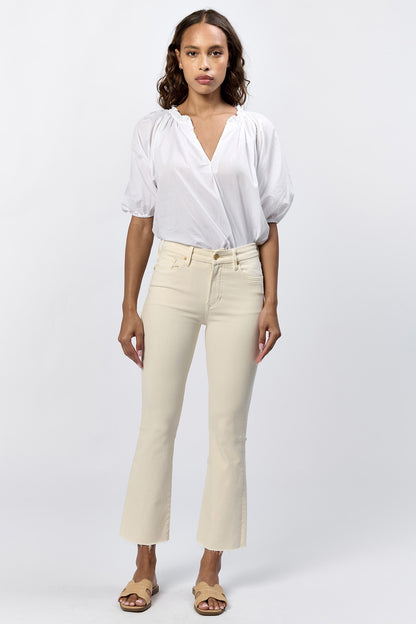 Full body view of a woman wearing the cream mid-rise raw hem flare jeans with gold hardware and a white top