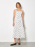 Front view of a model with short brown hair wearing a white midi dress with large black polka dots and black flats.
