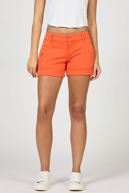 Front view of a woman wearing bright orange garment-dyed stretch shorts with a cuffed hem and white sneakers.