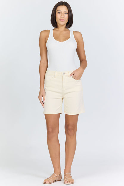 Full body view of a woman wearing cream-colored high-rise denim Bermuda shorts with flat tan strappy sandals.