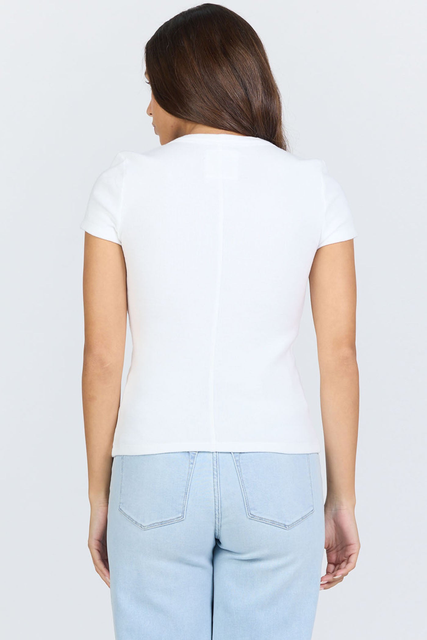 Rear view of a woman wearing a fitted white scoop-neck short-sleeve t-shirt tucked into blue jeans.