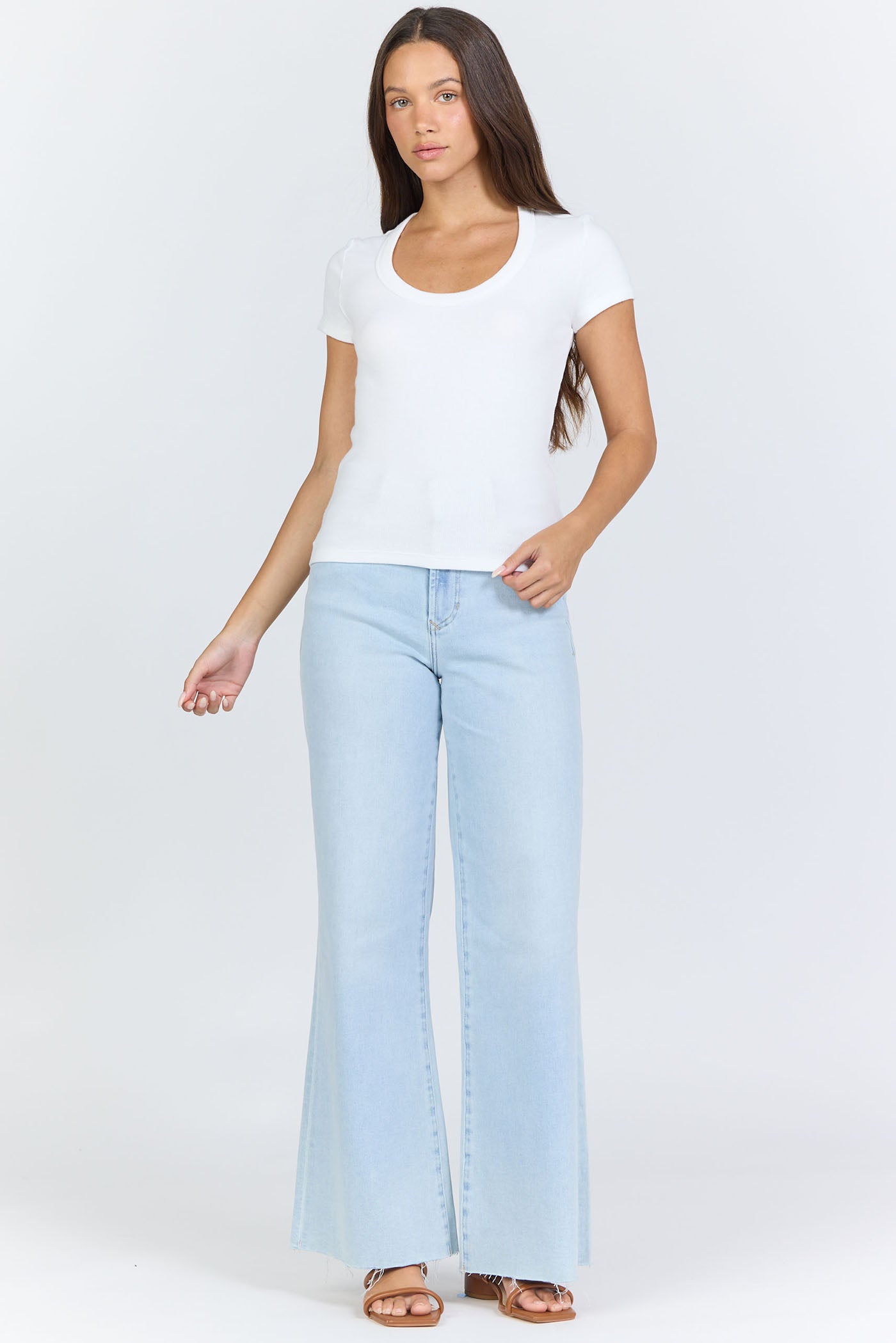 Full body view of a woman wearing a fitted white scoop-neck short-sleeve t-shirt tucked into blue jeans.