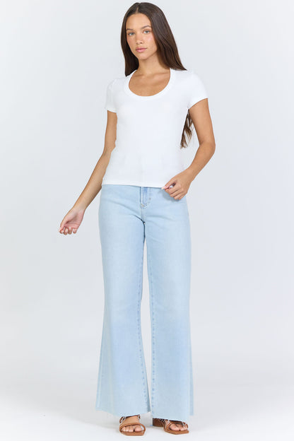 Full body view of a woman wearing a fitted white scoop-neck short-sleeve t-shirt tucked into blue jeans.